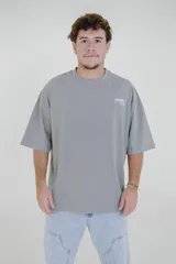 Remera gris de corte oversize con cuello redondo y estampado pequeño en el pecho con la frase "Karma Club" en color lila.