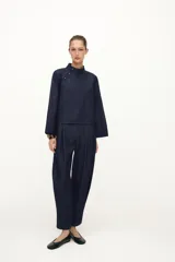 Pantalón de tiro alto confeccionado en denim oscuro, con pinzas delanteras que aportan volumen y pernera abullonada. Cuenta con bolsillos frontales, falsos bolsillos traseros con solapa y bajo ajustable mediante botones a presión.