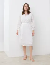 Vestido midi blanco de gasa labrada, con cuello a la base y escote en V. Cintura con lazo de ajuste, manga larga con puño elastizado y volado.