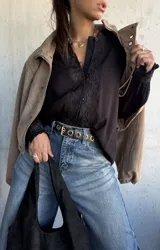 Camisa negra de corte holgado con detalles de encaje floral en la parte frontal y en los puños, cierre frontal con botones y cuello clásico.