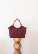 Cartera tipo tote de gamuza en color bordó, con asas cortas de cuero y correa larga desmontable. Cuenta con cierre superior y forro interior.