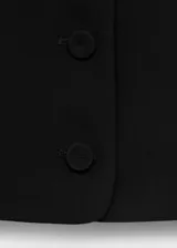 Chaleco negro de corte recto y estilo sastre, con cuello redondo abierto, tirantes anchos y cierre frontal de botones. Cuenta con forro interior completo.