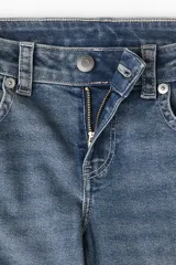 Jean de denim azul medio con leve efecto desgastado, corte ajustado hasta la rodilla y pierna acampanada (bootcut). Modelo de tiro bajo con cierre y botón, bolsillos abiertos delanteros y bolsillos traseros con solapa y botón.