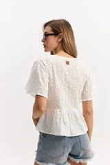 Blusa blanca de algodón con escote en V, mangas amplias y vuelo suave. Cuenta con un recorte en la cintura con frunce que aporta volumen y una caída fluida, además de una textura sutil con bordado inglés.