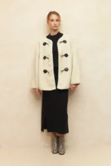 Abrigo gamulán de corderito color crudo, con alamares de cuero sintético negro y cierres metálicos.