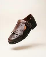 Mocasín de cuero natural color marrón, con costuras visibles, hebilla lateral metálica y solapa desmontable con flecos.