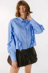 Camisa azul de algodón con volados en las mangas, cuello clásico y cierre frontal abotonado.