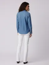 Camisa de manga larga en tela denim de color azul medio, con cuello clásico, botones frontales y dos bolsillos de parche con solapa en el pecho.