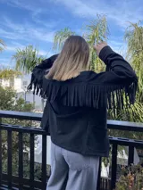 Chaqueta color beige de gamuza sintética con flecos en mangas y canesú, cuello camisero y cierre con botones.