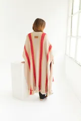 Ruana artesanal de tejido de punto, color beige con franjas horizontales gruesas rojas y finas amarillas. Posee flecos en el borde inferior.