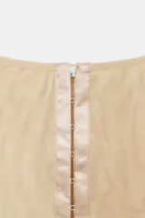 Top corsetero de tul semitransparente color beige, con escote cuadrado, tirantes anchos y cierre frontal con ganchos metálicos. Presenta bajo asimétrico y costuras reforzadas con ribetes a tono.