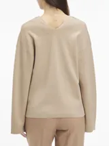 Sweater color beige de lana con escote en v, mangas largas y hombros caídos. Presenta logo de Calvin Klein en la parte superior trasera.