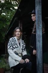 Saco tejido de largo medio con diseño de guarda inca en la parte superior y mangas. Presenta bolsillos con detalles bordados en cuero y flecos. Confeccionado en una mezcla de lana y poliamida.