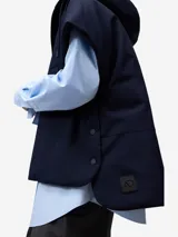 Chaleco acolchado de color azul marino, con capucha ajustable mediante cordón y cierre frontal de cremallera. Presenta bolsillos de vivo inclinados en el delantero y cierres laterales con broches a presión.