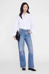 Pantalón jean de tiro alto y pierna recta amplia, color azul medio con efecto lavado. Presenta detalles de roturas sutiles a la altura de las rodillas y diseño clásico de cinco bolsillos.