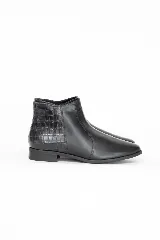 Botin de cuero negro con diseño combinado, presentando una parte frontal lisa y una parte trasera con textura de reptil. Posee suela baja y cierre lateral interno.