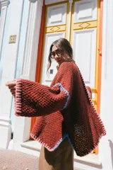 Saco oversize de tejido de punto en color beige, con mangas caídas y detalles de bordado a mano en tonos verde y lila en los bordes y costuras.