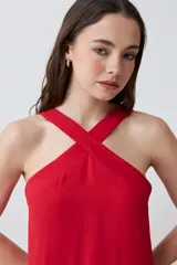 Vestido largo rojo, sin mangas, con escote halter cruzado en el frente y caída recta y holgada.