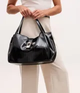 Bolsa tipo shopper de tamaño grande, confeccionada en poliuretano texturizado con acabado brillante. Presenta un diseño estructurado con correas fijas para el hombro, cierre superior mediante botón a presión y un detalle metálico decorativo en la parte frontal.