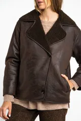 Campera tipo gamulan de corte oversize, color marrón oscuro con interior y solapas de corderito al tono. Presenta cierre frontal y mangas largas.