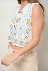 Chaleco de crochet sin mangas, con cuello estilo camisa y cierre frontal de botones. Diseño tejido con patrones geométricos en tonos blanco, celeste y verde oliva.