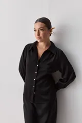 Camisa blanca de manga larga con textura suave y caída liviana, cuello camisero, puños anchos y fruncidos sutiles en los hombros.