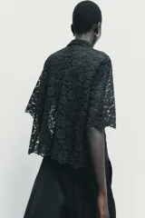 Camisa de encaje negro con cuello solapa, manga corta y cierre frontal con botones.
