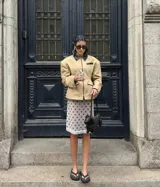 Chaqueta estructurada color beige con cuello, ribetes de bolsillos y detalles en negro. Presenta un diseño entallado con cierre frontal completo y hombreras marcadas.