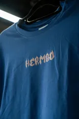 Remera azul con estampado frontal de la palabra "Hermod" en letras con efecto de fuego.