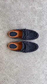 Zueco de cuero color azul marino, con diseño tipo mocasín destalonado, detalles de flecos en el empeine, cordones ajustables y plantilla en tono suela.