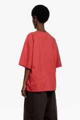 Camiseta negra de corte recto y largo medio, confeccionada en algodón orgánico. Presenta escote redondo, mangas cortas amplias con costuras raglán y detalles de cortes diagonales en el cuerpo.
