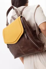 Mochila de cuero vacuno marrón con acabado pulido, solapa en forma de V y costuras decorativas. Cuenta con cremalleras laterales y asas ajustables.