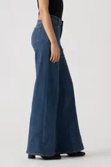 Jean de corte wide leg con costuras verticales frontales, tiro medio y cierre de botón y cremallera. Presenta un diseño de cinco bolsillos y trabillas para cinturón.