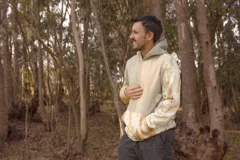 Canguro con capucha y cierre frontal, color beige con estampado de hojas en tonos marrones y amarillos. Mangas largas en color gris.