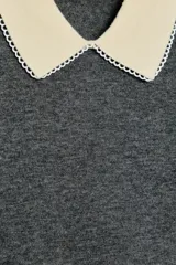 Polo de punto color gris oscuro con cuello y bordes de mangas en color crema, decorados con detalle de puntilla.