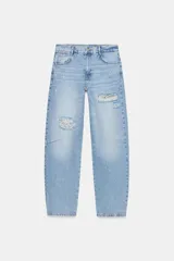 Jeans de tiro medio con corte baggy, pernera holgada que se estrecha hacia el tobillo. Presenta diseño de cinco bolsillos, cierre frontal con cremallera y botón, y detalles de roturas con aplicaciones de encaje en el frente.