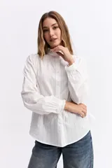 Blusa de algodón en color celeste, con textura sutil, cuello con volados y mangas largas con puños también decorados con volados. Presenta cierre frontal con botones.