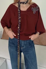 Jersey de punto color bordó con cuello asimétrico, detalle de nudo en el escote y pedrería en forma de hoja en el hombro. Manga larga.