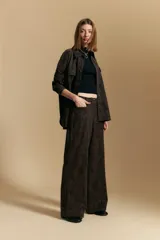 Pantalón de corte ancho y silueta relajada, confeccionado en tejido de efecto gamuzado color marrón oscuro. Presenta un diseño de tiro alto con cierre frontal y bolsillos laterales.
