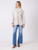 Cardigan beige con diseño de espiga, forrado en corderito sintético blanco. Presenta vivos en contraste color tostado en los bordes, cuello solapa y bolsillos tipo parche con solapa. Cierre frontal con botones carey.