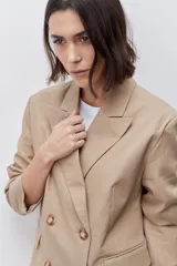 Blazer de silueta amplia y largo por debajo de la cadera, color café, confeccionado en tela suave y liviana. Presenta cuello con solapas, cierre cruzado con botones y bolsillos laterales con tapa.