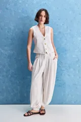 Pantalón de lino y viscosa color blanco, de tiro alto y calce holgado con pierna amplia, bolsillos laterales y puños ajustables con botones en los tobillos.