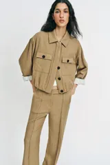 Chaqueta corta de color verde militar, con cuello solapa, bolsillos delanteros con solapa y cierre frontal de botones ocultos. Presenta mangas amplias con vuelta en los puños que muestran un forro a rayas.