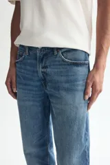 Jean de cinco bolsillos en denim de algodón con lavado medio y efecto desgastado. Modelo de cintura clásica con cierre y botón metálico, pierna recta y corte estándar.