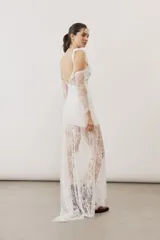 Vestido largo blanco de encaje con diseño asimétrico, tirante fino en un hombro y falda transparente.