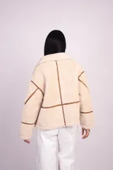 Campera de corderito color beige con ribetes y detalles en símil cuero marrón, cuello alto con hebilla decorativa, bolsillos laterales y cierre frontal.