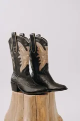 Botas tejanas de cuero negro con caña alta, taco cuadrado y delicadas costuras en contraste que forman diseños bordados en el cuerpo y empeine.