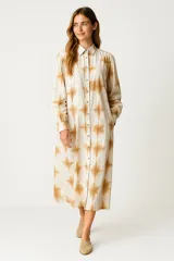 Vestido camisero midi de corte holgado, con cuello clásico, cierre frontal completo con botones y mangas largas con puños. Presenta un estampado geométrico tipo tie-dye en tonos beige y marrón.