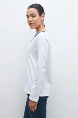 Remera blanca de manga larga con bordado floral azul en el escote.