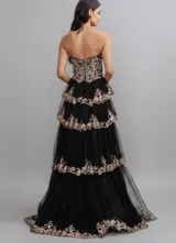 Vestido largo de fiesta con escote corazón y corset estructurado. Presenta un diseño de capas de tul con volados y bordados brillantes en tonos dorados sobre base negra. Incluye un tajo lateral profundo en la falda.